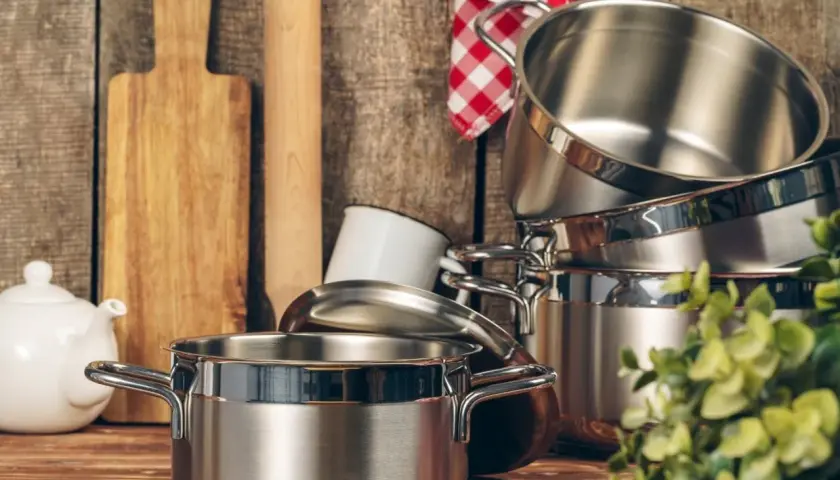 Ustensiles de cuisine en acier inoxydable 18/8, dont une casserole brillante, une théière blanche et des planches à découper en bois.