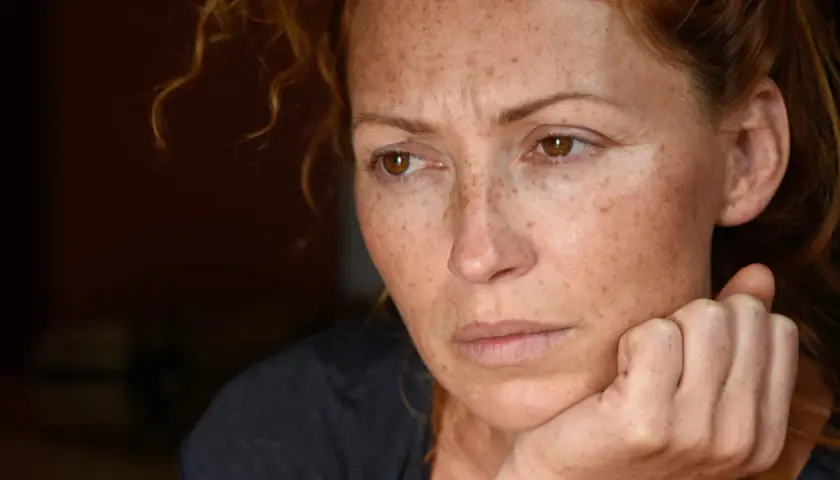 Portret kobiety z piegami, zamyślonej, z dłonią podpartą na policzku. Może odzwierciedlać 24 cechy wysoko wrażliwych osób.
