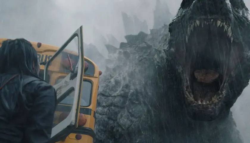 Enorm Godzilla vrålar mot en gul skolbuss i regnet, en del av **Monarch Legacy of Monsters**.