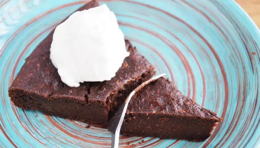 Pyszny brownie z cukinii codziennie fit, podane z bitą śmietaną na turkusowym talerzu.