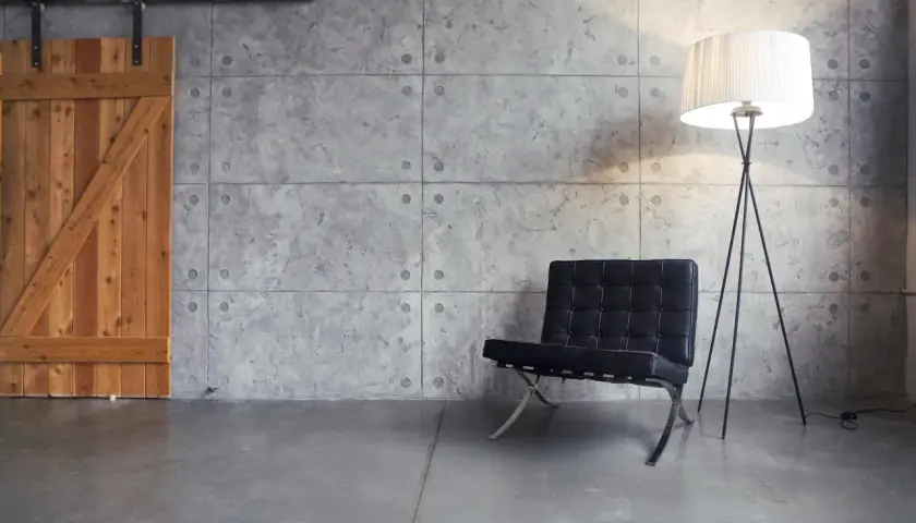 Drewniane drzwi przesuwne, czarny fotel i lampa stojąca na tle ściany z betonu dekoracyjnego.