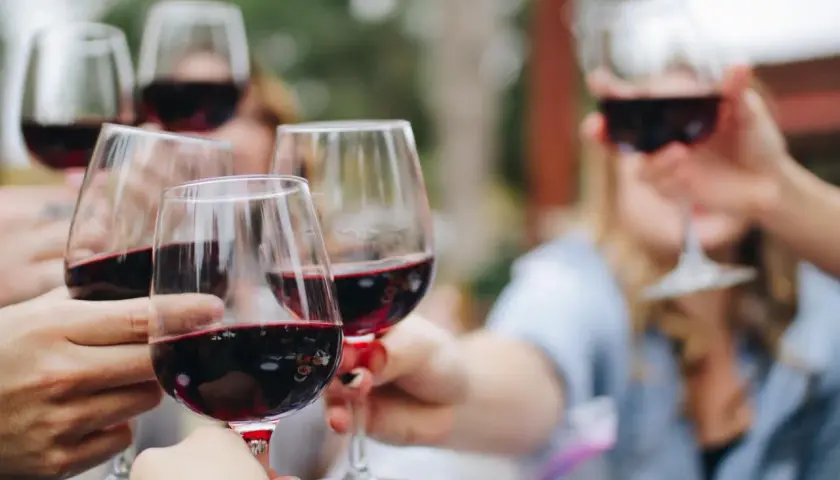 Des mains portent des verres de vin rouge pour un apéro convivial.