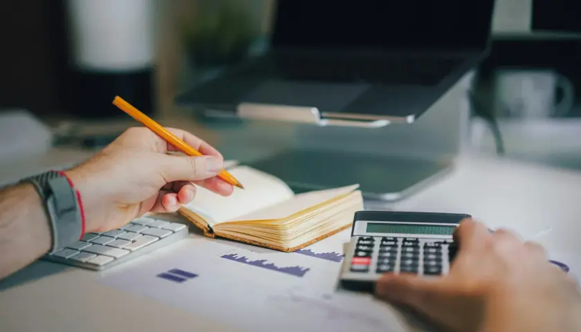 Un avocat postulant analyse des documents financiers avec un crayon, une calculatrice et un ordinateur portable.