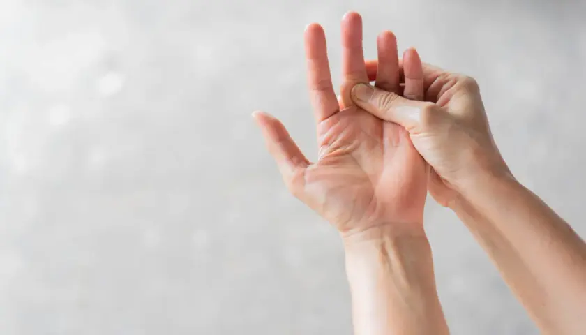 Eine Hand massiert den Bereich der Fingerknöchel, wo eine mögliche schnappfinger ursache liegen könnte.