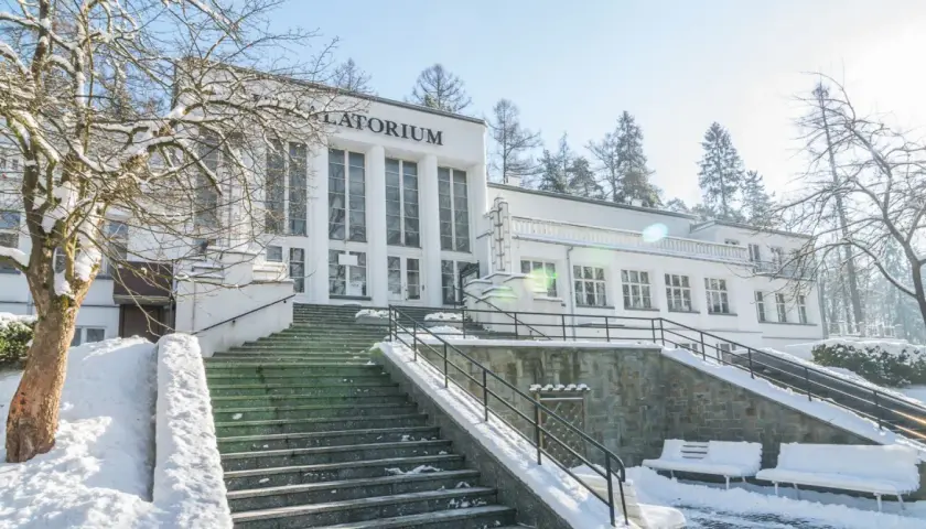 Zimowy dzień w Szczawnicy. Biały budynek sanatorium z napisem "Sanatorium" i schody pokryte śniegiem. Idealne miejsce na relaks w termach.