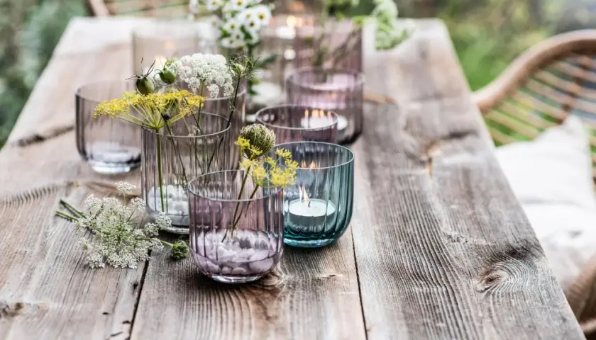 Romantische deko gartentisch mit Blumen und Kerzen in bunten Gläsern.