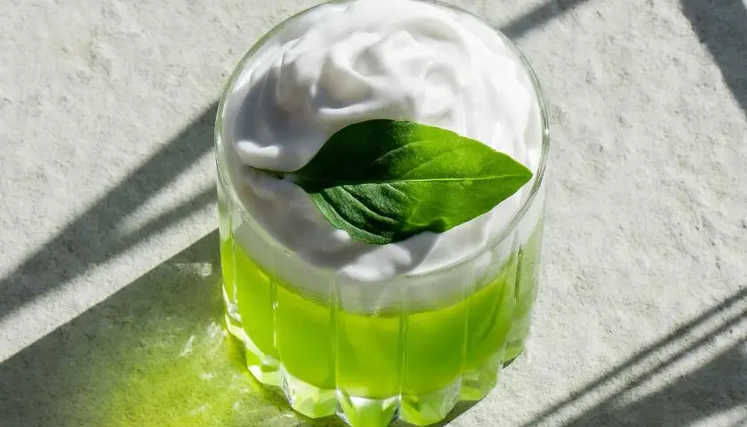 En grön thai basil drink med vitt skum och ett basilika-blad.
