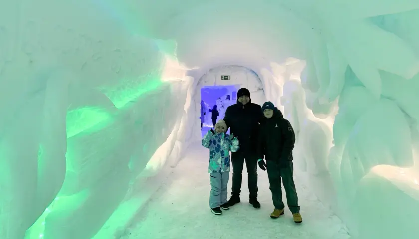 Rodzina w lodowym tunelu, gdzieś w okolicy wioski Świętego Mikołaja. Ściany lśnią zielonym światłem.