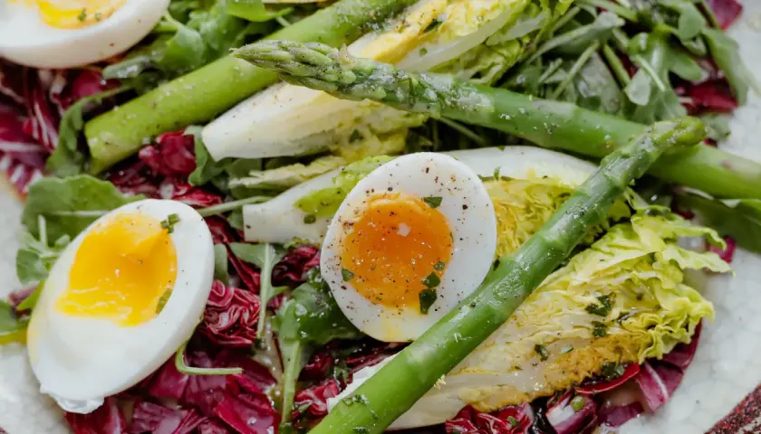 Salade colorée avec des œufs mollets, des asperges vertes croquantes et des feuilles de laitue et de radicchio.