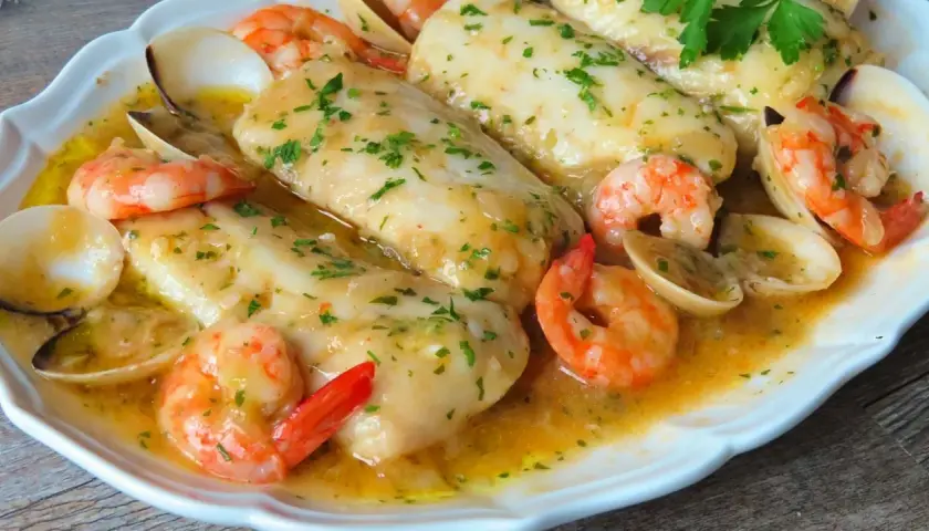 Merluza a la marinera con patatas, gambas y almejas en una salsa dorada.