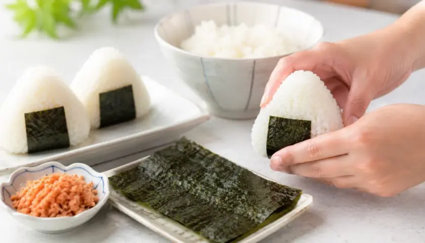 Dłonie formują pyszne onigiri. Obok miseczka z ryżem, nori i posypką.