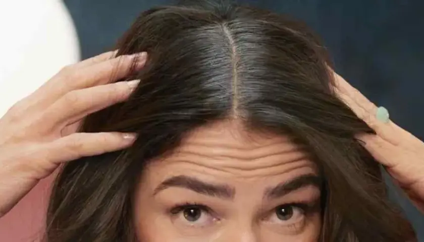 Mujer se toca el cabello oscuro, mostrando cómo disimular las canas en la raya.