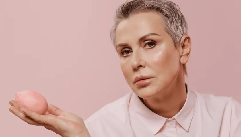 Femme aux cheveux gris et yeux marrons, maquillage subtil, tenant un objet rose.