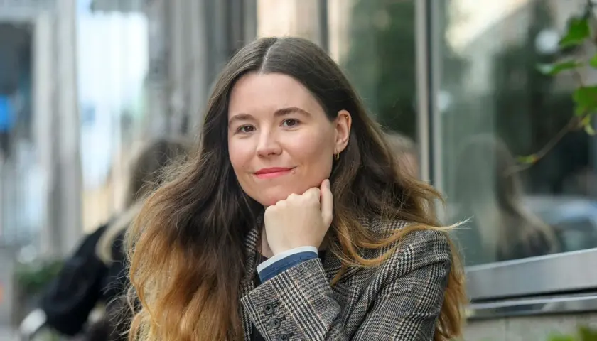 Johanna Hedman, med sitt långa, vågiga hår och en rutig kavaj, ler mot betraktaren.