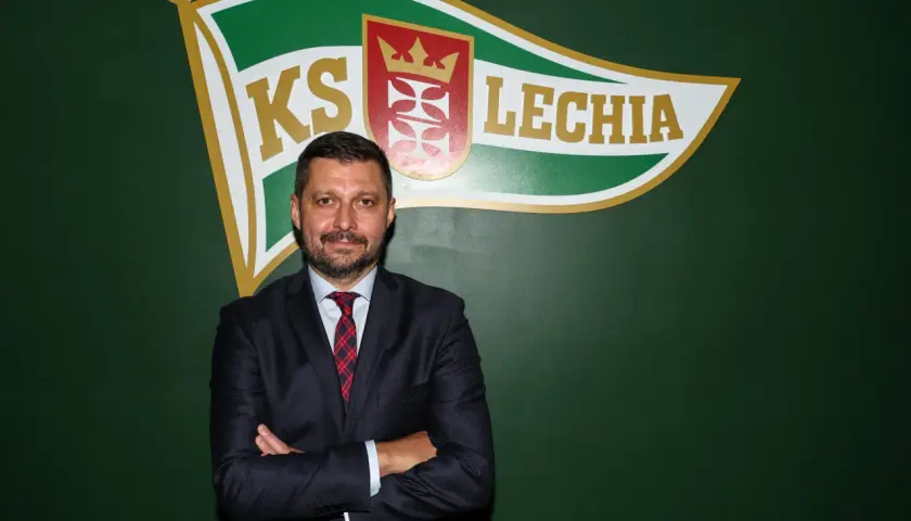 Marcin Kaczmarek, trener, stoi przed zieloną ścianą z logo Lechii Gdańsk.