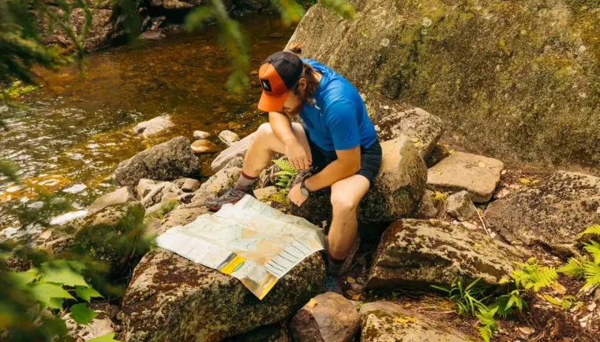 A hiker consults a map by a stream, perhaps planning his next move after some bushwhacking.