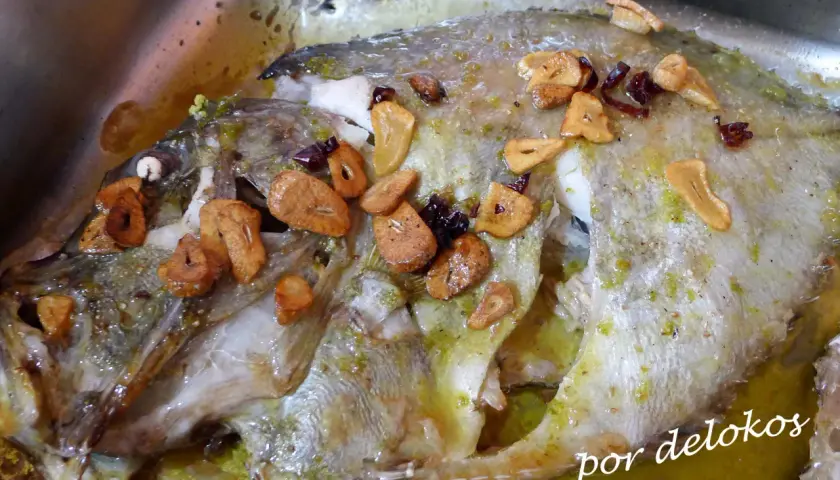 Un delicioso san martiño pescado al horno con ajo laminado y hierbas verdes, bañado en su jugo.