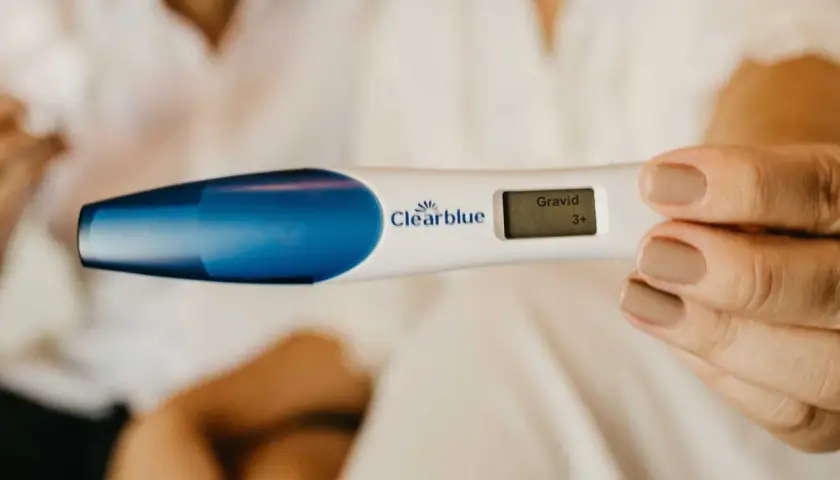 En kvinna håller en graviditetstest som visar "Gravid 3+". Kanske är det gravid andra barnet symtom som hon känner av.