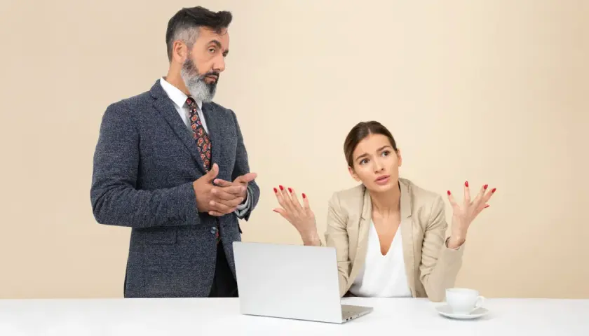 Un collega che vuole comandare, con un'espressione autoritaria, parla con una collega che sembra confusa e frustrata.