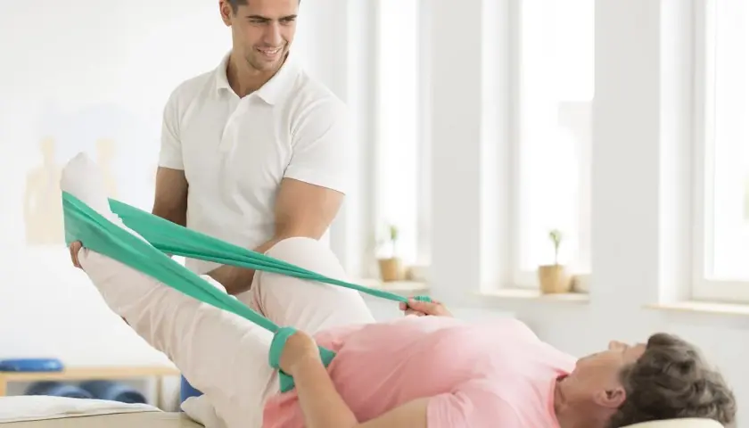 Fizjoterapeuta pomaga pacjentce w ćwiczeniach po endoprotezie biodra, używając taśmy rehabilitacyjnej do wzmocnienia mięśni.