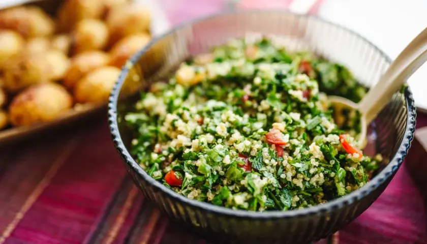 En skål med fräsch tabbouleh, perfekt för ett somrigt tabbouleh recept. Bredvid syns en bricka med små potatisar.