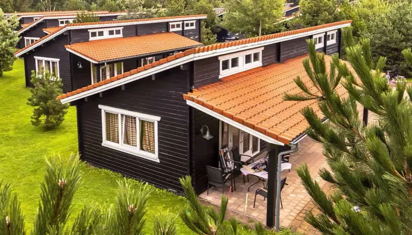 Czarny bungalow z pomarańczowym dachem, otoczony zielenią. Idealne miejsce na wakacje, co to za urok!