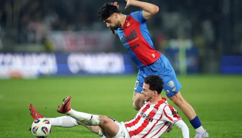 Piłkarz Cracovii w akcji, próbuje odebrać piłkę leżącemu zawodnikowi Piasta Gliwice. Intensywny przebieg meczu.