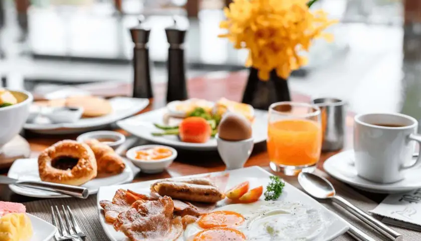 Desayuno abundante con huevos, salchichas, tocino y zumo de naranja, perfecto para tus viajes fin de semana baratos todo incluido.