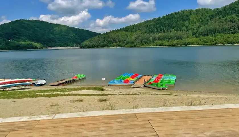 Plaża nad jeziorem Klimkówka. Rzędy kolorowych rowerów wodnych i kajaków czekają na turystów.