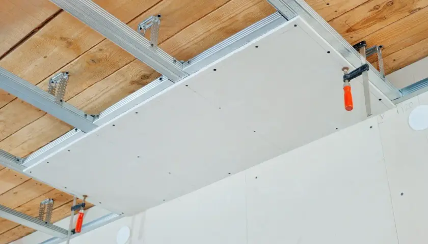 Installation d'un faux plafond en plaques de plâtre pour l'isolation phonique plafond appartement. Structure métallique fixée au plafond bois.