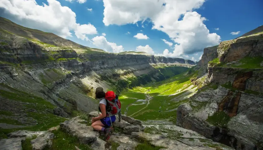 Senderista contempla el impresionante valle de Ordesa en Monte Perdido, Huesca, bajo un cielo azul con nubes algodonosas.