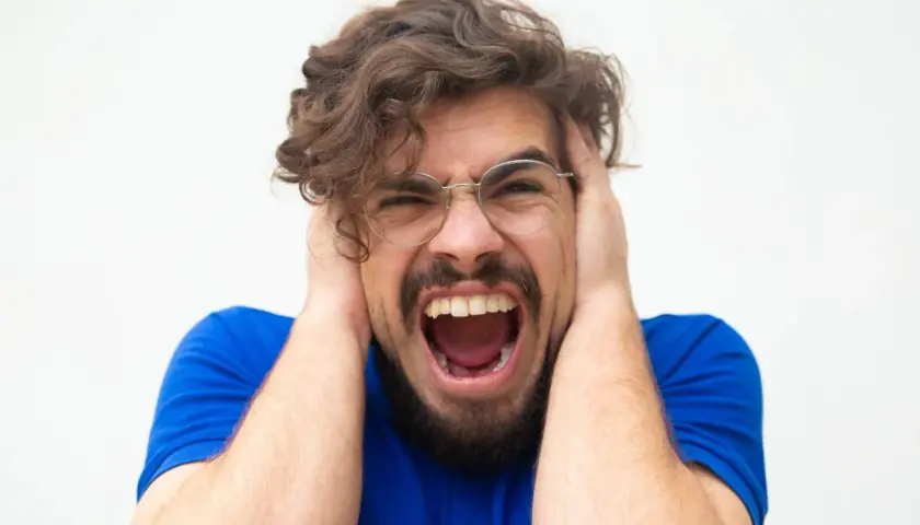 Uomo con mani sulle orecchie, urla disperato. Potrebbe essere un momento di attacchi di panico cosa fare per trovare sollievo.