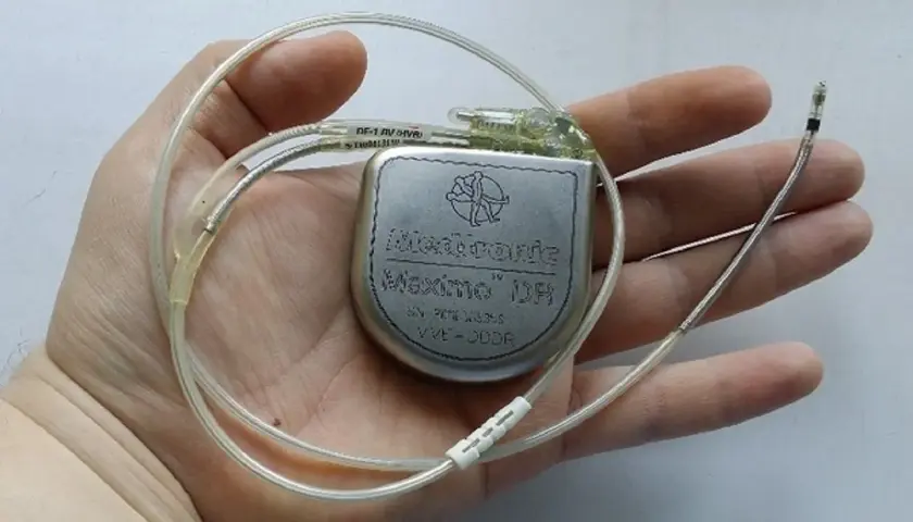 Dłoń trzyma kardiowerter Medtronic Maximo DR, urządzenie podobne do rozrusznika serca, z dwoma elektrodami.