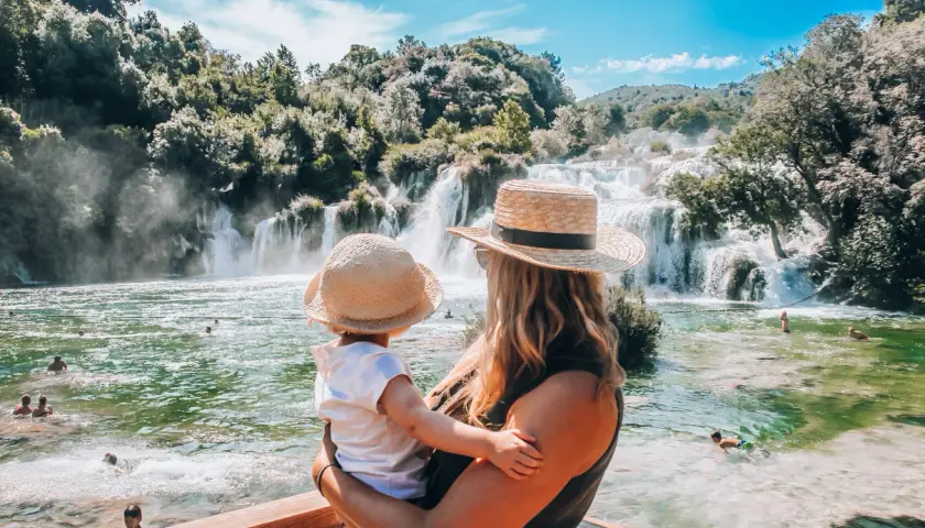 Mama z dzieckiem podziwia piękne wodospady Krka. Woda w rzece jest krystalicznie czysta, a wokół bujna zieleń.