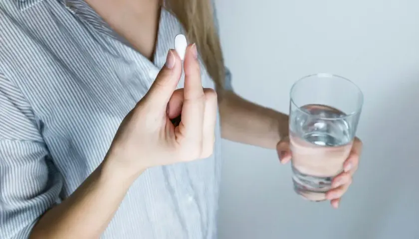 Donna tiene una pillola, forse un antibiotico per denti e gengive, accanto a un bicchiere d'acqua.