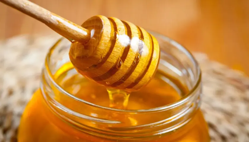 Ein Honigheber aus Holz tropft goldenen Honig in ein Glas. Kein Anzeichen von honig schimmel.