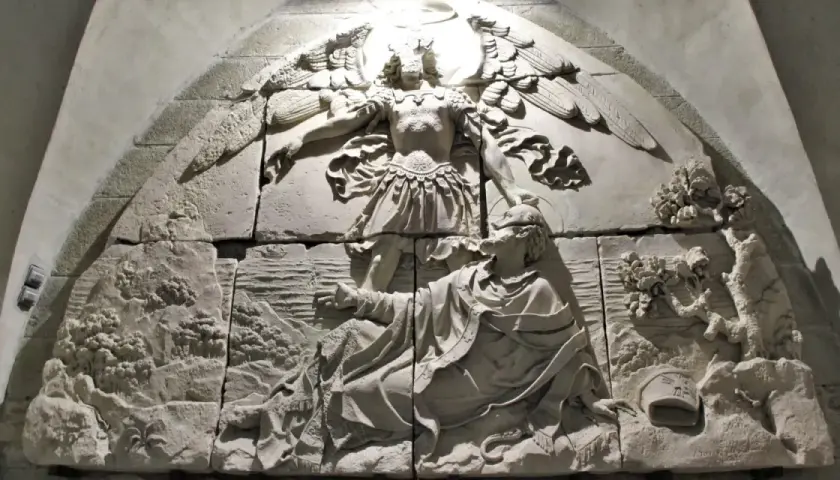 Relief mit Erzengel Michael, der einen Mann vor einem Drachen rettet. Die Szene zeigt die Namen der Erzengel in der Darstellung.