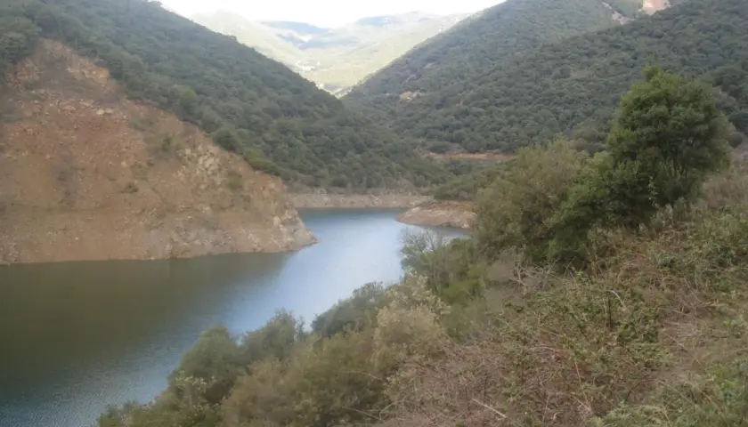 Embalse de Vallforners, un lago sereno rodeado de colinas verdes y rocosas, con vegetación densa en primer plano.