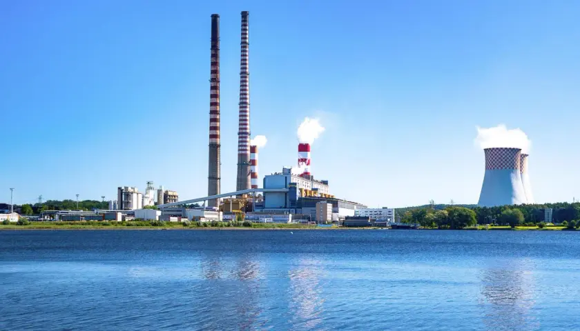 Elektrownia z kominami i chłodniami, odbijająca się w wodzie.