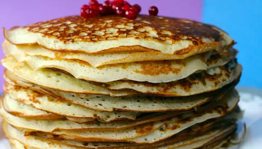 Pila di pancake senza farina, dorati e soffici, guarniti con bacche rosse.
