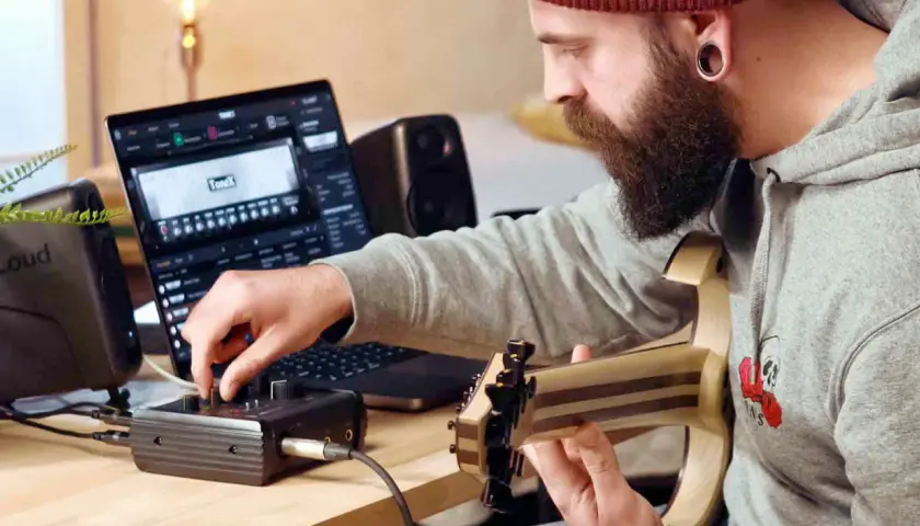 Mann mit Bart spielt Gitarre und bedient ein Audio-Interface, während er auf einem Laptop mit der **ToneX**-Software arbeitet.