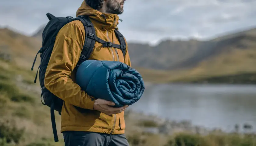 Hombre con mochila y saco de dormir enrollado, listo para elegir su aventura.