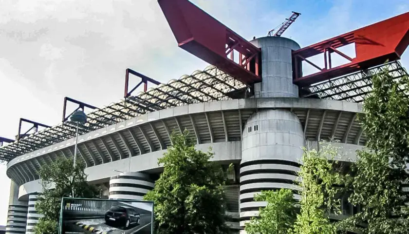Charakterystyczny stadion Interu Mediolan z czerwonymi elementami konstrukcji i zielenią wokół.