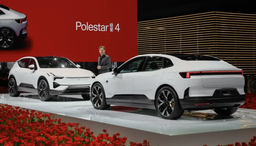 Dwa białe samochody Polestar 4 na scenie z czerwonym tłem i tulipanami.
