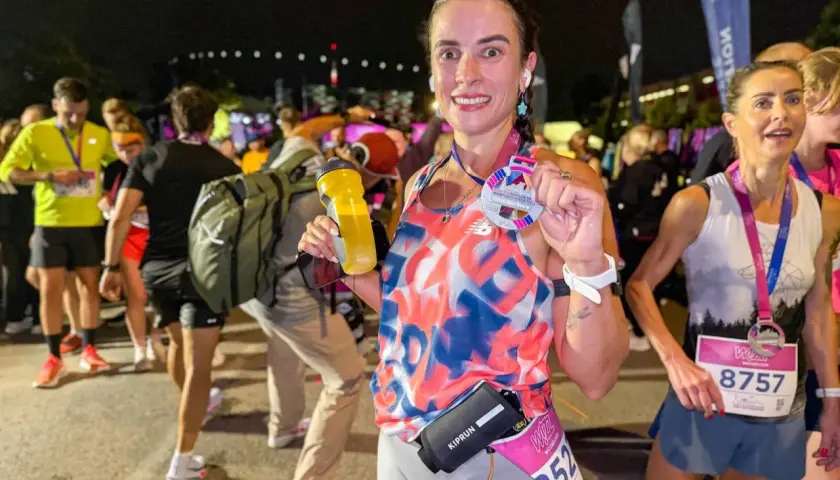 Uśmiechnięta biegaczka po ukończeniu biegu na 100 km, trzymająca medal i bidon.