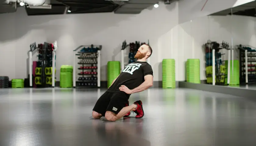 Mężczyzna wykonuje ćwiczenie nordic curl, klęcząc na podłodze i pochylając się do przodu.