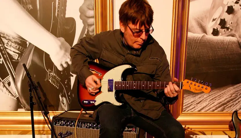 Mężczyzna w okularach gra na gitarze elektrycznej Fender, siedząc na wzmacniaczu.