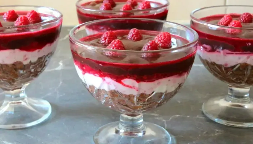 Pyszny deser z mascarpone i galaretką w pucharkach, udekorowany malinami. Idealny na letnie popołudnie.