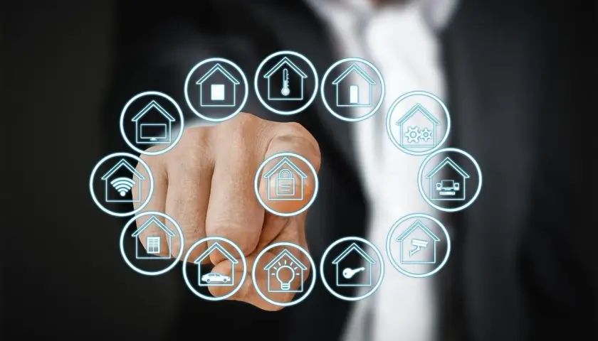 Dedo señalando iconos de casas que representan que es la domotica: seguridad, clima, luces, coche, wifi, TV, etc.