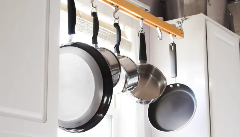Une astuce rangement casserolier : des poêles suspendues à une barre en bois, libérant de l'espace dans les placards.